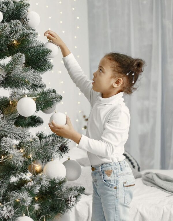 Niña decorando el árbol de Navidad con bolas blancas